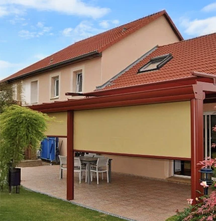 Terrasse couverte d'une maison résidentielle avec store banne beige déployé sous pergola métallique rouge
