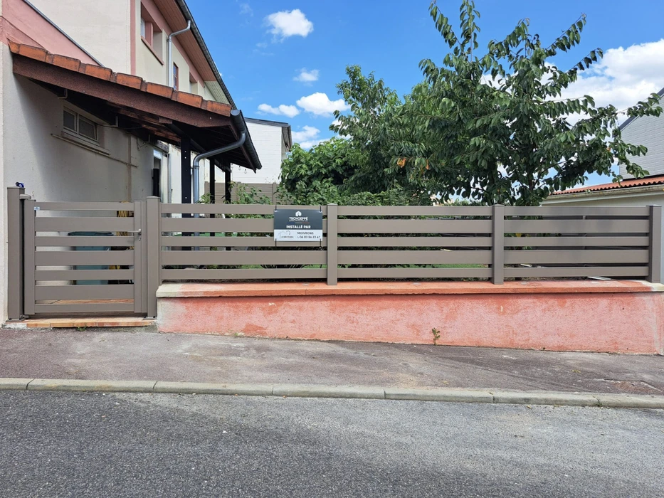 Clôture résidentielle moderne avec portail automatique coulissant gris anthracite, piliers en pierre naturelle beige, muret bas assorti