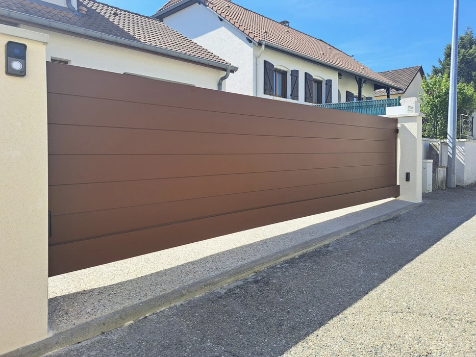 Portail coulissant blanc en PVC ou aluminium avec lames verticales ajourées, installé devant une maison pavillonnaire